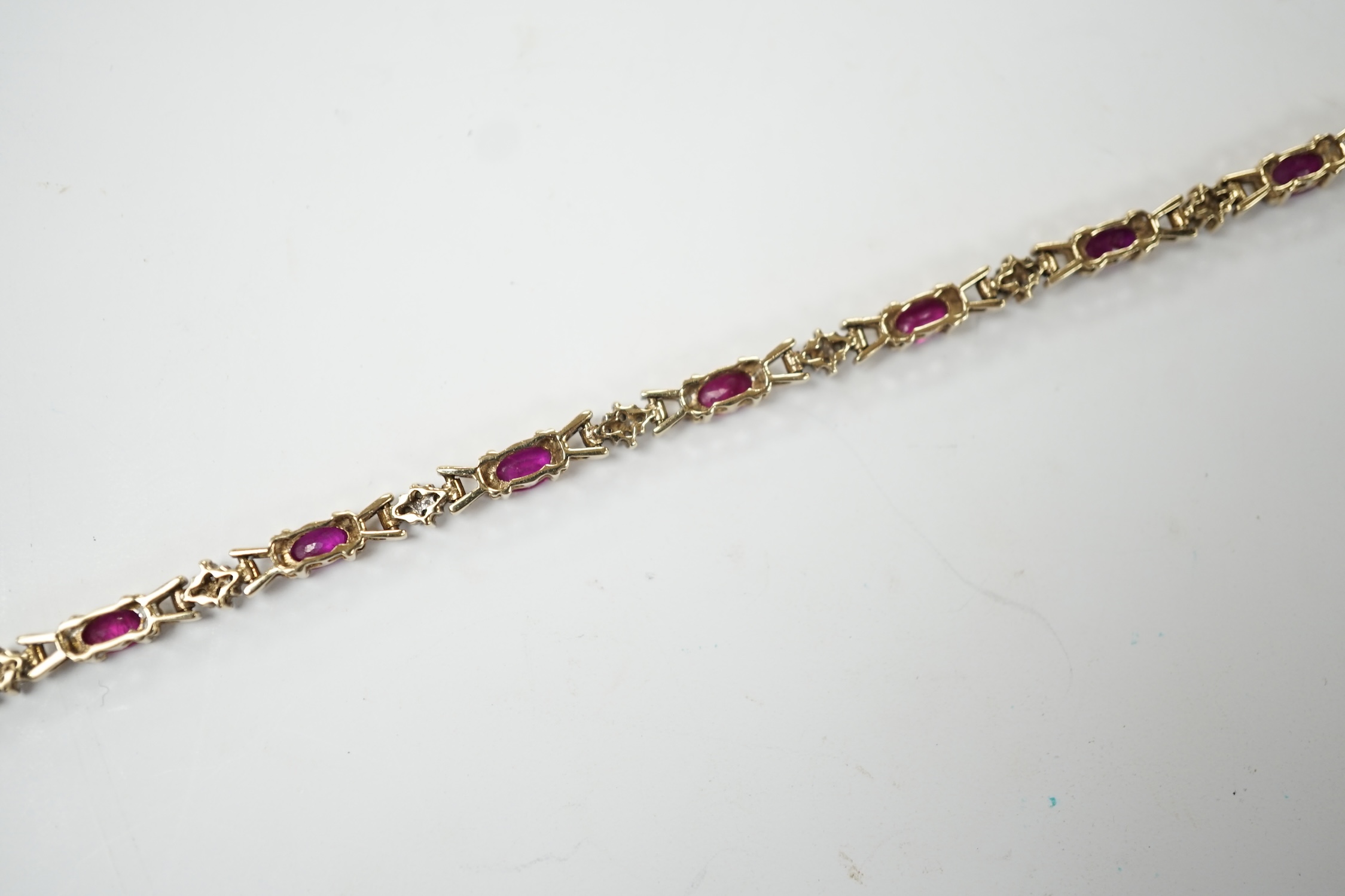 A modern 375 yellow metal, ruby and diamond cluster set line bracelet, 19cm, gross weight 7.6 grams. Fair condition.